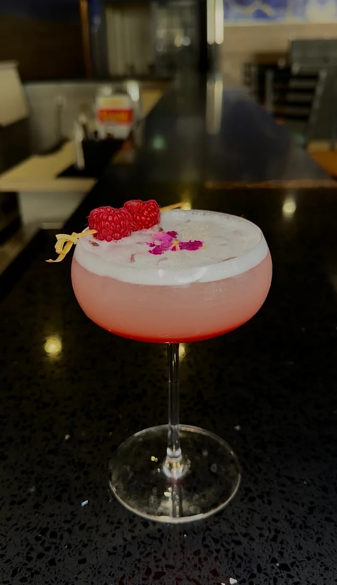 Pink coupe cocktail with foam and raspberries